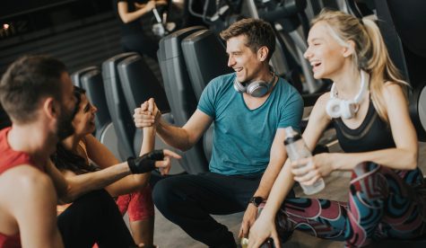Group pf young people in sportswear talking and laughing together while resting in the gym after a workout